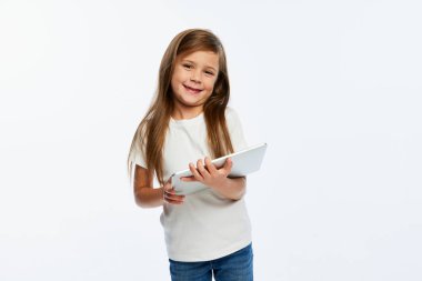 Neşeli, güzel küçük bir kız, beyaz arka planda izole edilmiş tablet kullanan günlük giysili bir öğrenci. Okuma, moda, okula dönüş kavramı. İlan için alanı kopyala