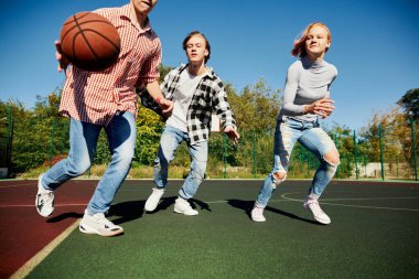 Gençlerden oluşan bir grup, basketbol sahasında sokak basketbolu oynayan öğrenciler ilkbaharda güneşli bir günde. Spor, eğlence aktiviteleri, hobiler, takım, arkadaşlık. Erkekler ve kızlar birlikte vakit geçiriyorlar..