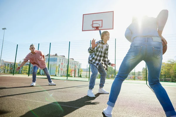 stock image Group of teens, students playing street basketball at basketball court outdoors at spring sunny day. Sport, leisure activities, hobbies, team, friendship. Boys and girl spending time together.