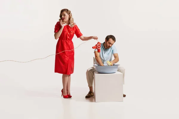 stock image Man washing dishes while woman talking on phone and holding hair dryer over water isolated on white background. Concept of retro style, domestic duties, old-fashion, lifestyle. Copy space for ad