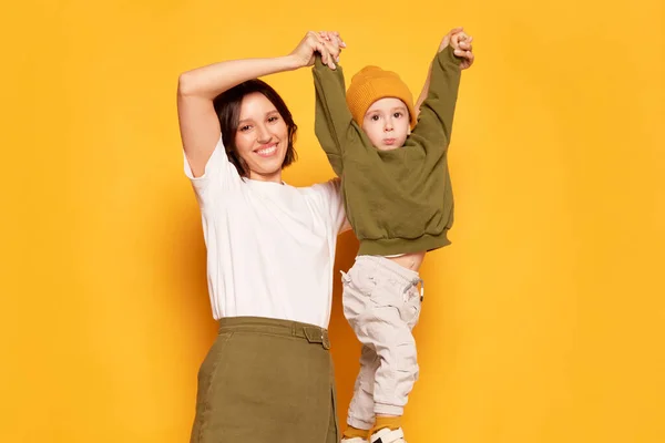 Fun, joy, play. Happy young mother with her cute little son having fun isolated on bright yellow background. Family, love, motherhood and Mothers day concept. Copy space for ad