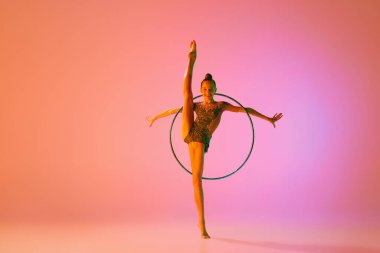 Genç ve çekici bir kızın stüdyo çekimi, neon ışık filtresiyle izole edilmiş spor ekipmanlarıyla ritmik jimnastik eğitimi. Dans, müzik, duygular, zorluklar, motivasyon ve reklam