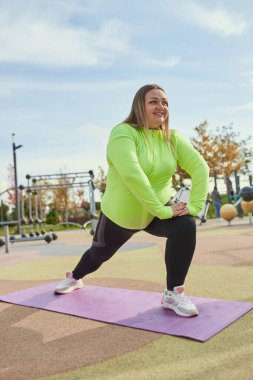 Pozitif tutum en iyi sonucu elde etmek için yardımcı olacaktır. Enerjik obez genç kadın, baharda güneşli bir günde spor salonunda spor giyim antrenmanı yapıyor. Meydan okumalar, hayaller, fitness, sağlıklı