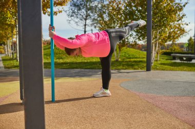 Antrenmandan sonra esneme hareketleri. Enerjik obez genç kadın, baharda güneşli bir baharda spor sahasında spor kıyafetleriyle antrenman yapıyor. Zorluklar, hayaller, fitness, sağlıklı yaşam tarzı kavramı