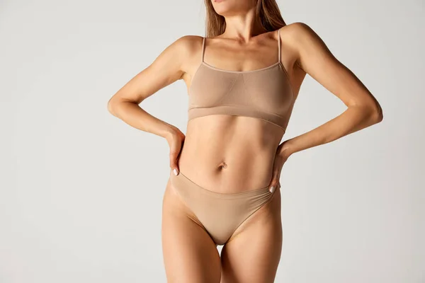 Cropped image of slim female body, breast and belly over grey background. Womans health care. Model in underwear. Concept of beauty, body and skin care, health, plastic surgery, cosmetology, diet