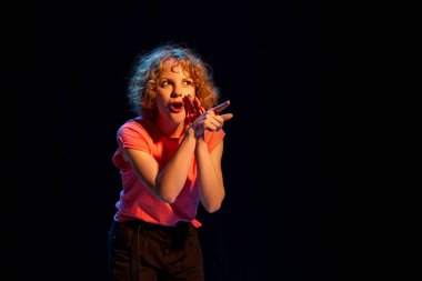 Siyah arka planda izole edilmiş birini işaret eden kısa kıvırcık saçlı, duygusal genç bir kız. Yüz ifadeleri, pozitif ve negatif duygular ve vücut dilleri kavramı