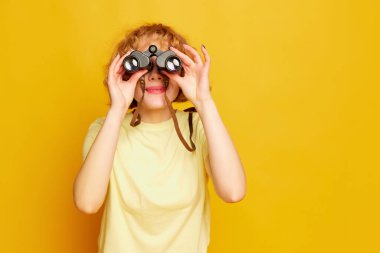 Yeni vizyon. Sarı stüdyo arka planında izole edilmiş dürbünle bakan neşeli, güzel, kızıl saçlı bir kadın. Gelecek, hedef, satış, reklam. İnsani duygular, yüz ifadesi, güzellik kavramı.