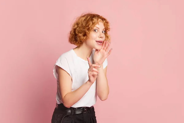 美丽的红头发女子在粉红的工作室背景上窃窃私语 人类的情感 面部表情 美的概念 为广告复制空间 模特儿看上去很神秘 — 图库照片