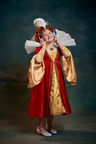 红头发小女孩的肖像 皇室成员用深绿色背景的耳机听音乐 历史重制的概念 中世纪时尚 女王的比较 — 图库照片