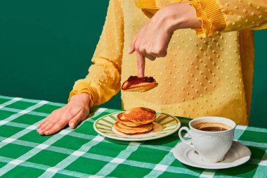 Tatlı krep ve yeşil masa örtüsünün üstünde reçelli kahvaltı yapan bir kadın. Antika, retro tarzı iç mekan. Yemek ve sanat fotoğrafçılığı. Tamamlayıcı renkler. İlan, metin için boşluk kopyala