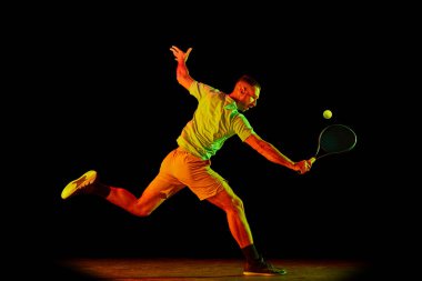 Athlete playing tennis. Young sportive man, professional tennis player in motion, action isolated over dark background in neon light. Concept of professional sport, competition, skills. clipart