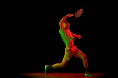 Tenis oynayan profesyonel tenisçinin karanlık arka planda neon ışıkta izole edilmiş görüntüleri. Eylem kavramı, başarılar, moda, hobiler, hareket ve profesyonel spor.