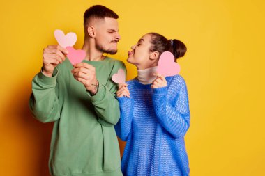 Güzel genç bir çiftin portresi, kadın ve erkek poz veriyor, komik suratlar yapıyor, sarı arka planda somurtuyor. Aşk kavramı, ilişki, Sevgililer Günü, duygular, yaşam tarzı, kutlama