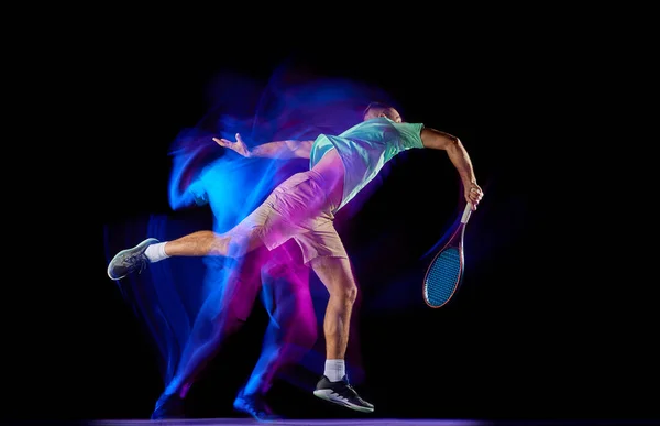 Tシャツを着た若い男性テニス選手と 混合紫ネオンライトで暗い背景に隔離されたテニスをしているショートパンツ プロスポーツの概念 — ストック写真
