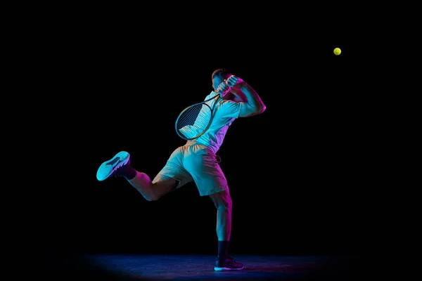 選手はテニスをする 若いスポーツマン 運動中のプロのテニス選手 ネオンライトの暗い背景の上に隔離されたアクション プロスポーツ スキルの概念 — ストック写真