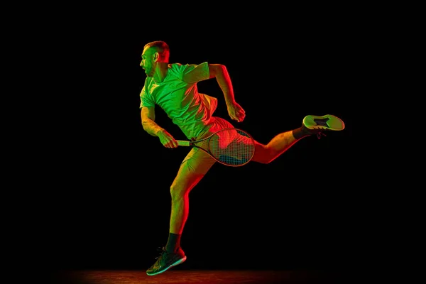 エネルギーとパワー ネオンの光の中で暗い背景に隔離されたテニスをプレイスポーツウェアで精力的な男性テニス選手のダイナミックな肖像画 プロスポーツの概念 — ストック写真