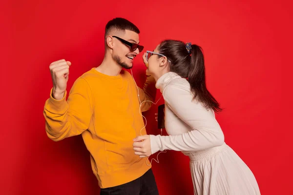 一对快乐的年轻夫妇的画像 男人和女人 用红色背景的耳机一起听音乐 爱的概念 情人节 生活方式 — 图库照片