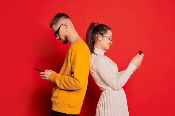 一对快乐的年轻夫妇的画像 男人和女人 头戴耳机 背靠背地站着 背对着红色背景的电话 爱的概念 情人节 生活方式 — 图库照片