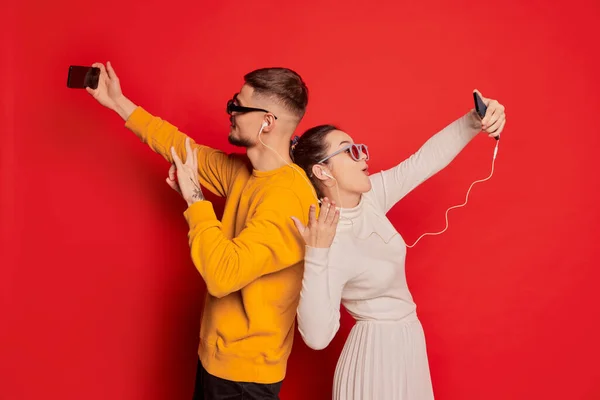 幸せな若いカップル 男と女の肖像画 後ろに立ち 赤い背景の上に隔離された電話でビデオ通話をしている バレンタインデー ライフスタイルの概念 — ストック写真