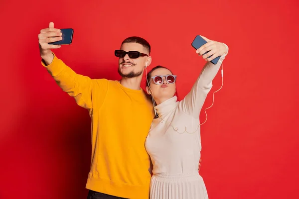 一对快乐的年轻夫妇的画像 男人和女人 摆出姿势 拿着自己的手机 背景是红色的 看起来很开心爱的概念 情人节 生活方式 — 图库照片