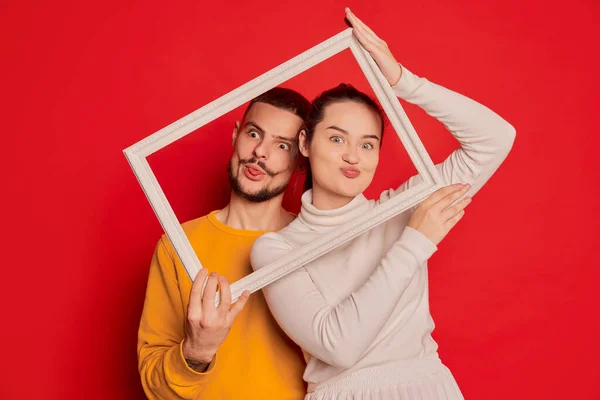 幸せな若いカップル 男と女の肖像画は 赤い背景に隔離された面白い顔を作る 画像フレームでポーズ バレンタインデー ライフスタイルの概念 ぎゅっと — ストック写真