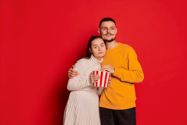 一对快乐的年轻夫妇的画像 男人和女人 摆姿势 看与爆米花隔离红色背景的电影 爱的概念 情人节 生活方式 — 图库照片