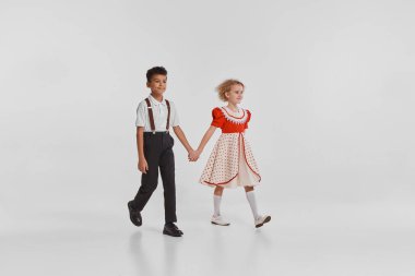 Güzel küçük çocukların portresi, klasik elbiseli kız ve erkek el ele tutuşup gri arka planda izole bir şekilde yürüyorlar. Çocukluk kavramı, yaratıcılık, eski moda, arkadaşlık, sanat