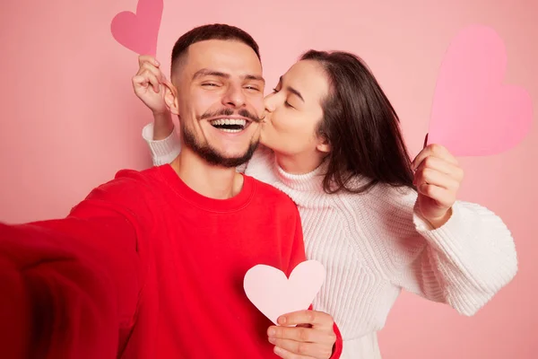 美しい若いカップルの肖像画 女性は幸せと笑顔の男にキス ピンクの背景に隔離された一緒に自撮りを取ります バレンタインデー ライフスタイルの概念 — ストック写真