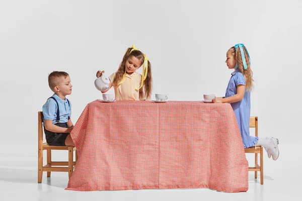 三个孩子的画像 男孩和女孩 把茶倒进杯子里的女孩被灰色的背景隔开了 一起举办茶话会童年 创造力 复古时尚 艺术的概念 — 图库照片