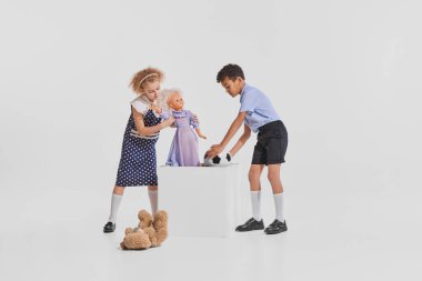 İki çocuğun portresi, oyuncak bebekle oynayan kız, gri arka planda izole edilmiş futbol topuyla oynayan oğlan. Çocukluk kavramı, yaratıcılık, eski tarz, eski moda, arkadaşlık, sanat