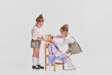 İki küçük kızın portresi, oyuncak bebekle oynayan çocuklar, saçlarını tarayan gri arka plan. Çocukluk kavramı, yaratıcılık, eski tarz, eski moda, arkadaşlık, sanat