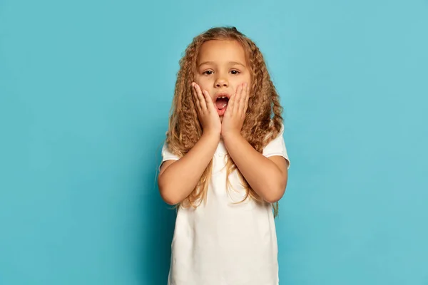 令人惊讶的孩子可爱的小快乐的女孩 孩子长卷曲的头发看着相机孤立的蓝色背景 儿童的正面情感 面部表情的概念 广告的复制空间 — 图库照片