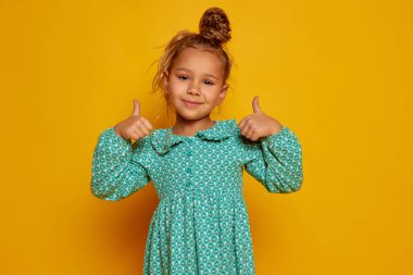 Gülümseyen çocuk. Sevimli küçük mutlu kız, uzun kıvırcık saçlı çocuk sarı arka planda izole edilmiş kameraya bakıyor. Çocukların olumlu duyguları, güzelliği, yüz ifadeleri kavramı. İlan için alanı kopyala