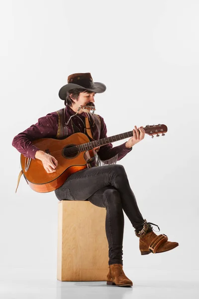 카우보이 스타일의 기타와 하모니카를 연주하는 남자의 초상화가 배경에서 고립된 공연하고 — 스톡 사진