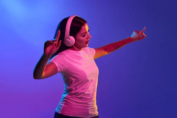 いい音だ 閉じて若い女の子は ネオンの光の中で青とピンクの色の背景に隔離された白いヘッドフォンで学生 ファッション 勉強の概念 — ストック写真