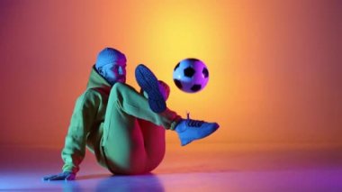 Kafkasyalı profesyonel futbolcu futbol topuyla bacaklarında hokkabazlık yapıyor, neon ışığı var. Profesyonel futbolcunun stüdyo çekimi, modern şehir gençlik kıyafetleri giyen adam. Spor, serbest stil