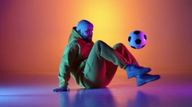 Kafkasyalı profesyonel futbolcu futbol topuyla bacaklarında hokkabazlık yapıyor, neon ışığı var. Profesyonel futbolcunun stüdyo çekimi, modern şehir gençlik kıyafetleri giyen adam. Spor, serbest stil