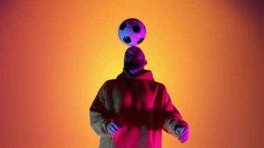 Kafkasyalı profesyonel futbolcu futbol topuyla kafa üstü, neon ışıklı hokkabazlık yapıyor. Profesyonel futbolcunun stüdyo çekimi, modern şehir gençlik kıyafetleri giyen adam. Spor, serbest stil