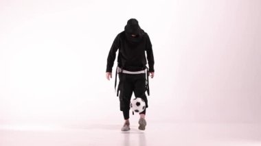 Genç erkek oyuncu yerdeki beyaz stüdyoda futbol topuyla hokkabazlık yapıyor. Kafkasyalı profesyonel futbolcu. Modern şehir gençlik kıyafetleri giymiş bir erkek ya da erkek. Spor, spor, serbest stil konsepti
