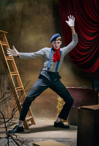 Retro circus show. Vintage portrait of male mime artist expressing sadness and loneliness over dark retro circus backstage background. Concept of emotions, art, fashion, style