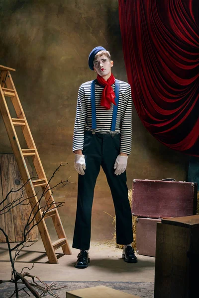 Retro circus show. Vintage portrait of male mime artist expressing sadness and loneliness over dark retro circus backstage background. Concept of emotions, art, fashion, style