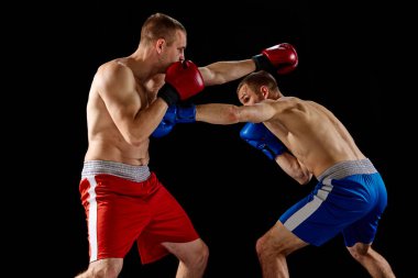 Dövüş. Karanlık arka planda izole edilmiş spor üniformalı iki profesyonel boksörün dinamik portresi. Spor anlayışı, rekabet, eğitim, enerji. Sporcular motive olmuş, aktif görünüyorlar