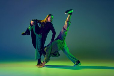 Duygular harekete geçti. İki dansçı, renkli mavi-yeşil arka planda neon ışıkta çağdaş dans eden modaya uygun dans çifti. Sanat kavramı, yaratıcılık, hareket, moda