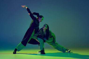 Duygular. Gündelik kıyafetlerle dans eden zarif genç kızlar neon ışıklarıyla dans eden dans salonundaki mavi-yeşil arka planda dans ediyorlar. Gençlik kültürü, çağdaş dans, moda, aksiyon.