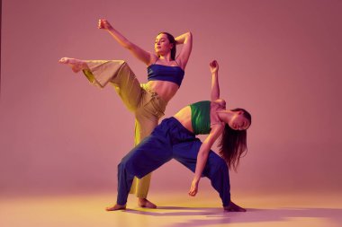 Kristal pembe arka planda hareketli ve hareketli çağdaş dans çifti. Genç, şık, şık kızlar dans ediyor. Modern sanat, moda, gençlik tarzı ve yaratıcılık kavramı