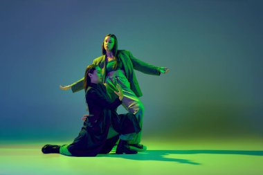 Duygular harekete geçti. İki dansçı, renkli mavi-yeşil arka planda neon ışıkta çağdaş dans eden modaya uygun dans çifti. Sanat kavramı, yaratıcılık, hareket, moda