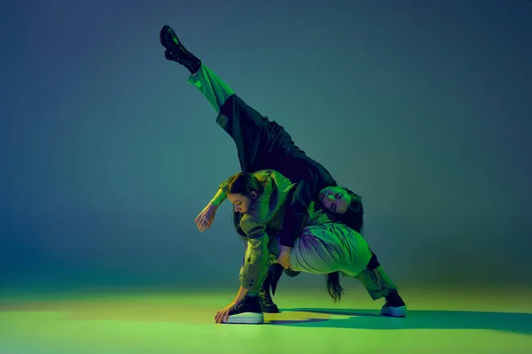 モダンダンスのコンセプト ネオンの光の中でグラデーションの青緑の背景でコンテンポラリーダンスを踊る2人の若い女性の精力的なカップル 創造性 ファッションの概念 — ストック写真