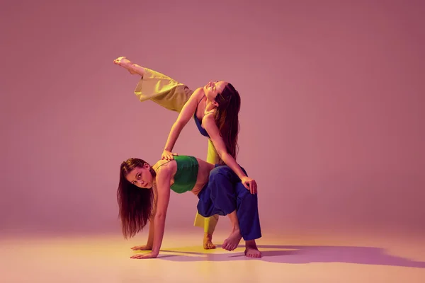 stock image Energetic dancers in art performance at dance hall. Young stylish fashionable girls dancing isolated on crystal pink background. Concept of modern art, fashion, youth style and creativity