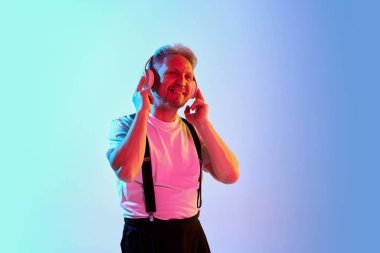 Tişörtlü olgun bir adamın portresi, kulaklıkla müzik dinlemek neon rengi mor arka planda izole edilmiş. Duyguların kavramı, yüz ifadesi, yaşam tarzı, moda. İlan için alanı kopyala