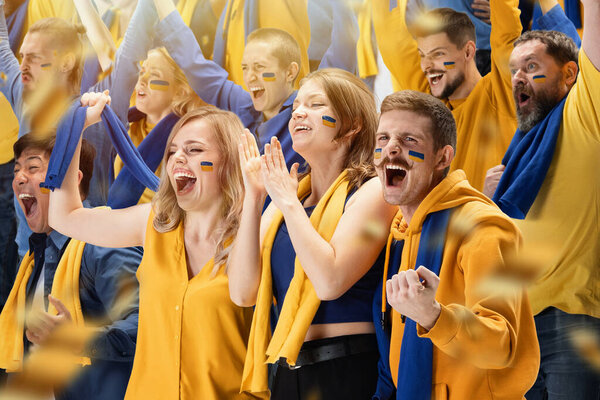 Shouting. Group of young people, thrilled soccer football fans cheering for national sport team at stadium. Concept of emotions, global sports competitions, championship, ad. Blue and yellow colors